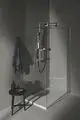 Duschbereich mit klaren Wänden und einer Handbrause von Ideal Standard. Handtuch hängt an der Wand, ein kleiner Beistelltisch steht daneben. Minimalistische Gestaltung in gedeckten Farben.
